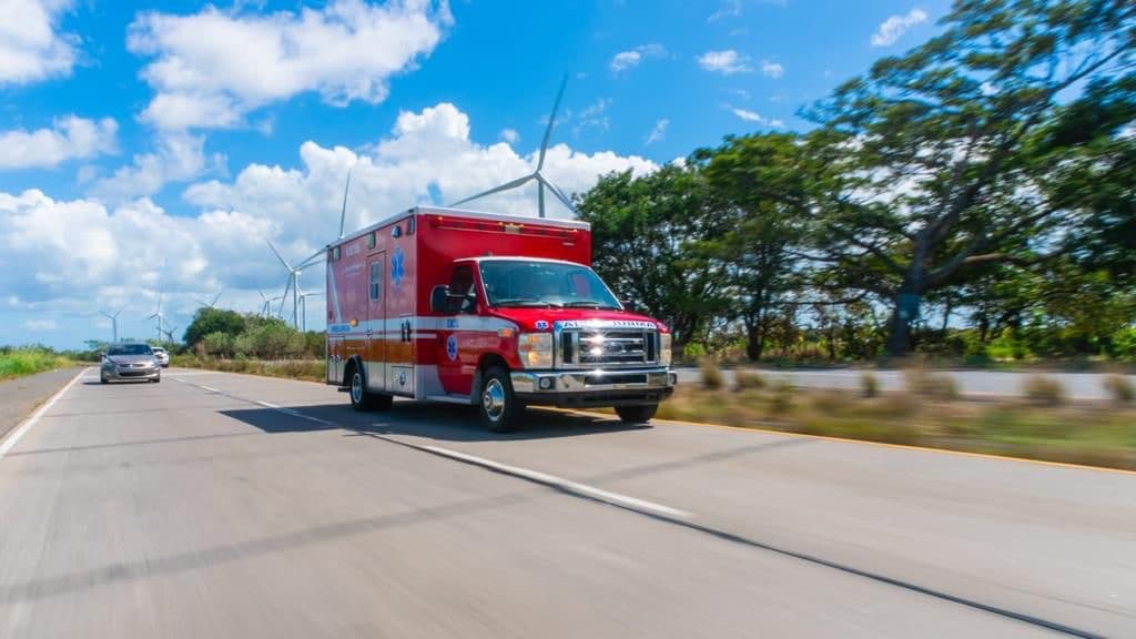 An EMTS ambulance responding on the highway past a wind farm